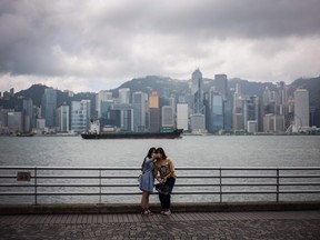 Two women pose for a selfie next to the Star Ferry pier in Victoria Harbour as clouds loom over the skyline of Hong Kong