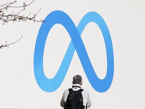 A person stands in front of a Meta sign outside of the company's headquarters in Menlo Park, Calif.