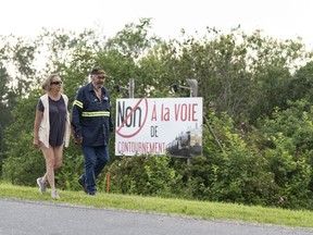 Rita Boulanger and Raymond Savoie walk past a sign stating "No to the bypass" on their property in Lac-Mégantic on July 6, 2023. The couple faces losing their home as the federal government plans to expropriate land from some residents in Lac-Mégantic and surrounding towns to build a rail bypass to remove trains from the town's downtown area.