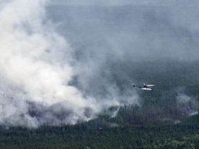 A helicopter carrying a water basket flies past a smoke plume near Lebel-sur-Quévillon, Que., Wednesday, July 5, 2023.