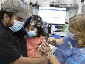 Vincent Garneau holds his four-year-old daughter, Simone, as she gets her first shot of the COVID-19 vaccine at the Décaire Square vaccination centre in Montreal on Monday, July 25, 2022. A health-care worker blows bubbles and plays with Simone as she receives the vaccination.