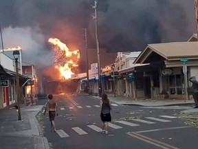 People watch as smoke and flames fill the air from raging wildfires on Front Street in downtown Lahaina, Maui on Tuesday, Aug. 9, 2023.