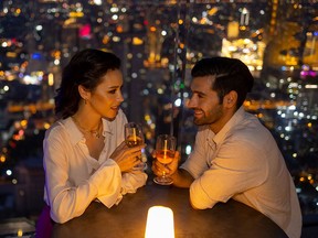 Caucasian couple celebrating holiday event at luxury rooftop bar at night.