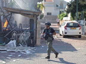 A member of the Israeli forces runs past a fire rages in a house in Ashkelon, following a rocket attack from the Gaza Strip on southern Israel on October 7, 2023.