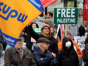OTTAWA. OCTOBER 25, 2023. A man flies a Canadian Union of Postal Workers (CUPW) flag alongside pro Palestinian signs at a "Stand with the Global Strike for Palestine" rally in front of the Human Rights Monument in Ottawa.