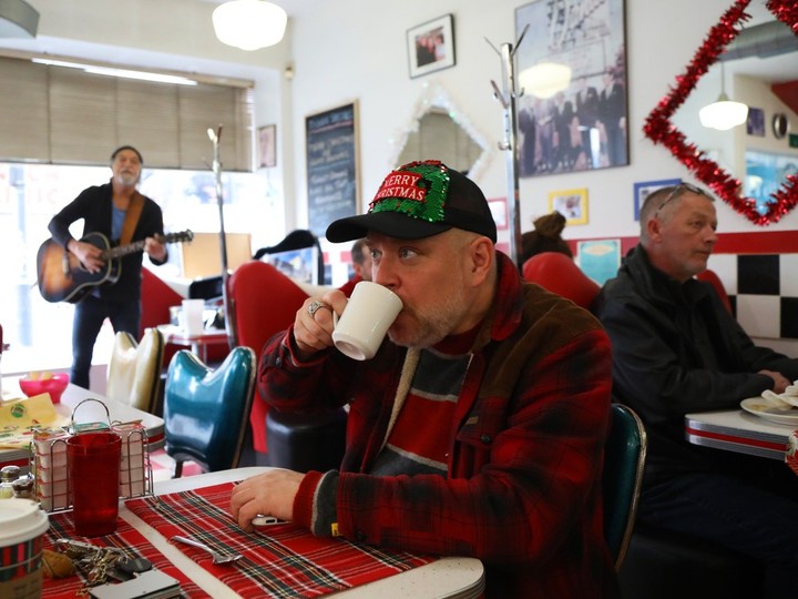  David Kirk enjoys a cup of coffee at the Bramasole Diner on Christmas Day while musician Victor Nesrallah performs.