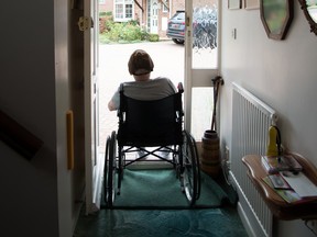 Man in wheelchair stares out door of house