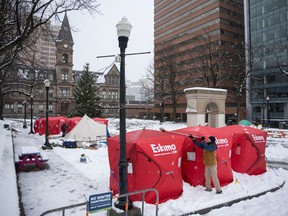 Matthew Grant uses a broom to clean snow off ice fishing enclosures at a tent encampment in front of City Hall in downtown Halifax's Grand Parade square, Monday, Dec. 4, 2023.