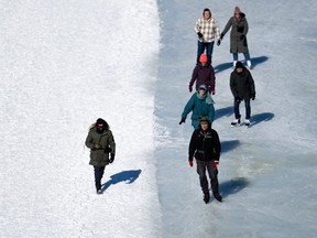A person walks beside skaters on the edge of the Rideau Canal Skateway in Ottawa, on Family Day Monday, Feb. 19, 2024. The National Capital Commission (NCC) has reopened the outdoor skateway from Bank St., to Pretoria Bridge with skating conditions being described as 'variable'.