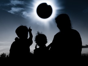 Silhouette back view of mother and children sitting together, watching to solar eclipse on dark sky background.