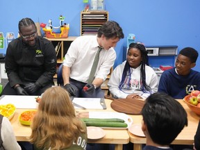 Prime Minister Justin Trudeau talks to ten year old Chakai as he cuts fruit next to chef Jason Simpson while preparing food for a lunch program at the Boys and Girls Club East Scarborough, in Toronto, Monday, April 1, 2024. Trudeau says the upcoming federal budget will include funding for a national school food program that aims to provide meals to 400,000 more kids per year across the country.