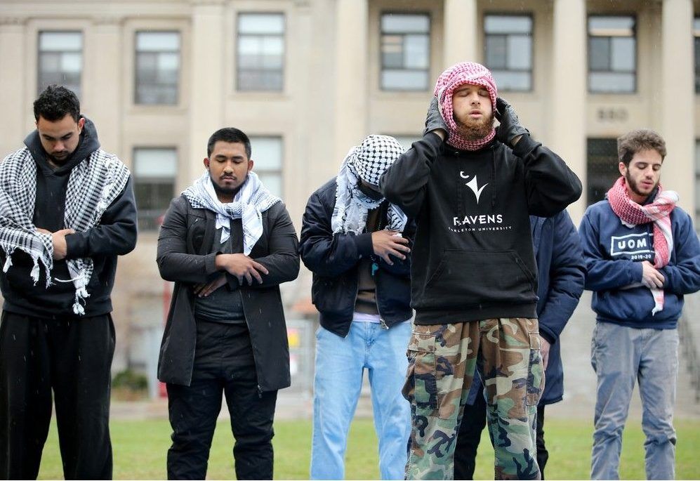 Six young men go about their daily prayers on the lawn of Taberet Hall on Tuesday. A gathering of about 20 protesters were set up outside Tabaret Hall at the University of Ottawa