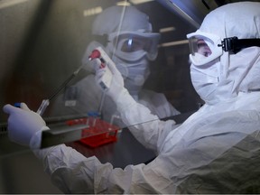 A manufacturing associate takes a sample while working under a clean hood in the biotherapeutics lab's virus manufacturing centre at the The Ottawa Hospital