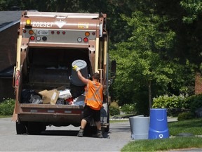A city worker wearing an orange vest empties a garbage can in a garbage truck