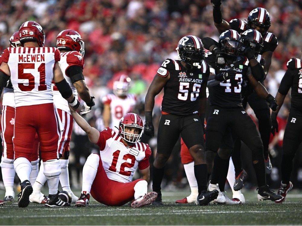 Calgary Stampeders quarterback Jake Maier (12) is helped up as Ottawa Redblacks linebacker Davion Taylor (43) celebrates his sack