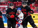 Tomas Galvas, de la República Checa, queda atrapado entre el canadiense Tanner Howe (23) y su compañero de equipo Andrew Gibson (2) mientras mueve el disco sobre el hielo durante el juego mundial juvenil previo al torneo en Ottawa, el lunes 23 de diciembre de 2024.