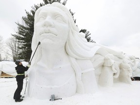 Someone smooths the facade of a snow sculpture of a woman with flowing hair