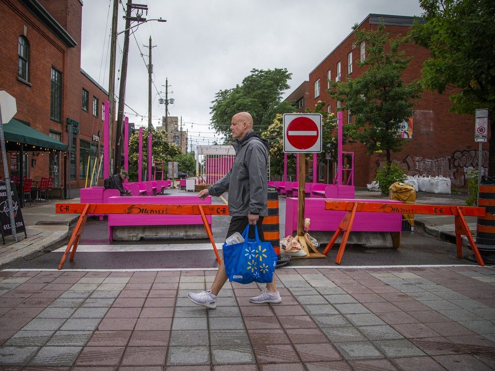  People sit and walk past temporary seating areas at the intersections of along Bank Street in Ottawa, part of the Street Seats pilot program that closes sections of the road to vehicles.