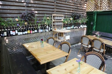 Wine bottles line the side of a patio with wooden tables in the shade