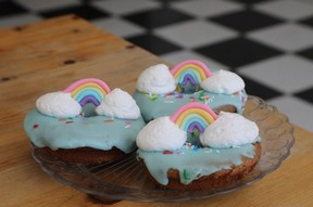 Three donuts with light blue icing topped with fondant rainbows over fluffy whipped cream clouds