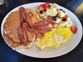 A plate with pancakes, bacon, scrambled eggs and fresh fruit