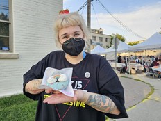 Someone wearing a face mask holds up a rainbow donut in front of an outdoor night market