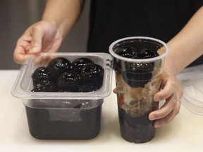 A container filled with giant boba next to a tall plastic cup
