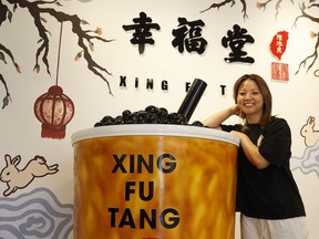 Someone in a black shirt leans on a giant bubble tea in front of a mural with bunnies, cherry blossoms and hanging lanterns