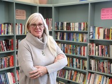 Someone with long white hair stands in front of shelves full of books