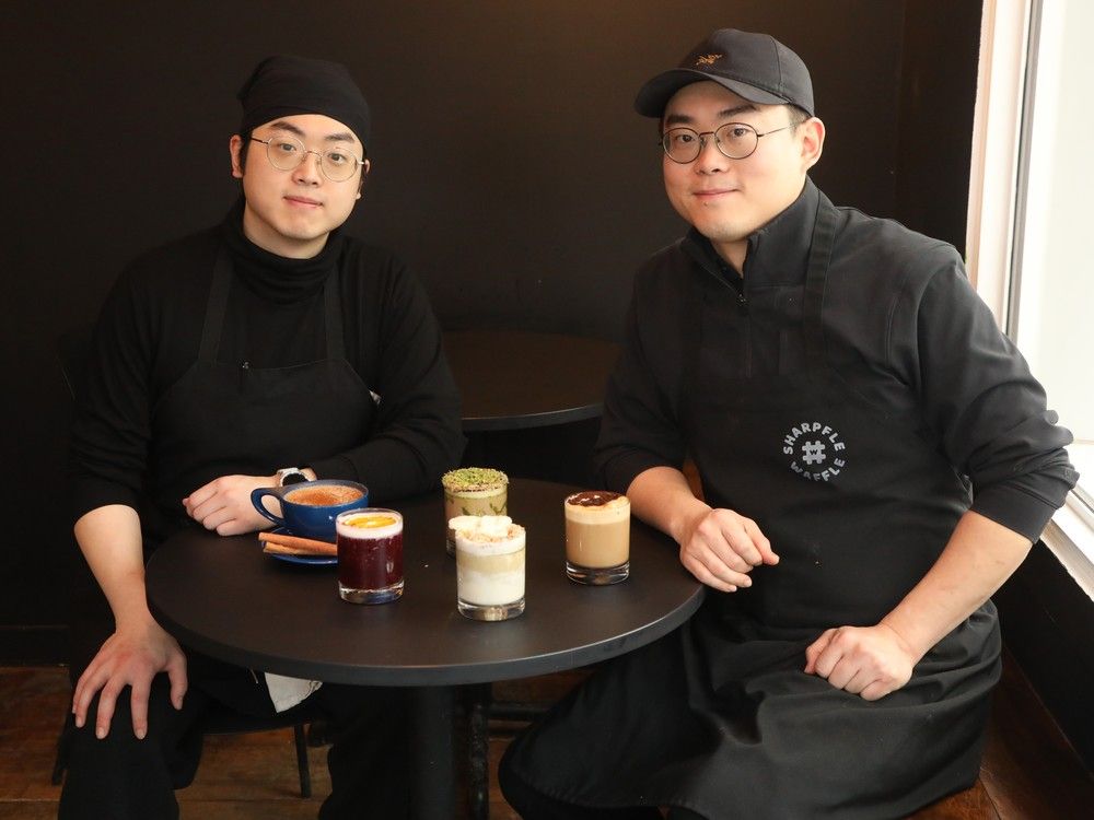 Two people in all-black outfits sit in front of a table with a lineup of drinks