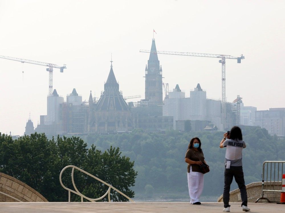 Suzannah is photographed in front of Parliament Hill by her friend Chan, both visiting from Vancouver. Suzannah was wearing a mask due to the wildfire smog that lay over Ottawa on June 6, 2025.