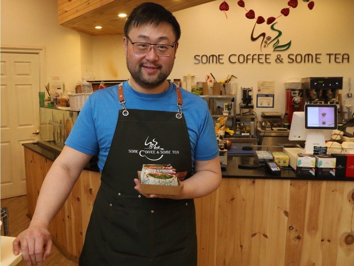Someone in an apron holds a sandwich in front of a cafe counter