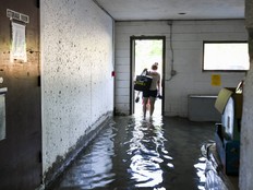 A resident of a McEwen Avenue apartment building treads through water as they evacuate with their belongings following severe flooding and thunderstorms on July 1.
