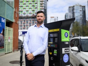 A man in a light blue button up leans up against a parking metre.