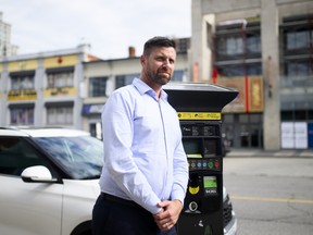 A man in a light blue button up leans up against a parking metre.