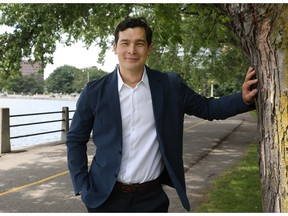 A man in a blue suit and white undershirt leans against a tree