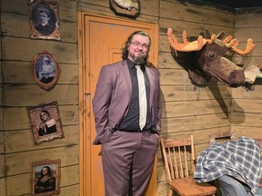Someone in a suit stands near a puppet moose head on the cabin wall