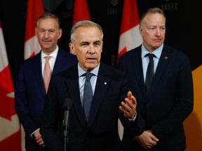 Prime Minister Mark Carney, joined by CEO of Defence Investment Agency Doug Guzman (left), and Secretary of State (Defence Procurement) Stephen Fuhr (right) speaks to members of the media at CANSEC in Ottawa in May.