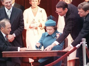 Queen Elizabeth signs Canada's constitutional proclamation as Michael Pitfield, clerk of the Privy Council, points and prime minister Pierre Trudeau looks on. On the right is Michael Kirby, then secretary to cabinet on federal-provincial relations.