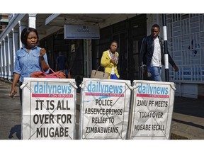 Pedestrians walk past a newspaper stand on a street in downtown Harare, Zimbabwe Sunday, Nov. 19, 2017. Zimbabwe's ruling party Central Committee says longtime President Robert Mugabe must resign as president by noon Monday or impeachment proceedings will start. (AP Photo/Ben Curtis) ORG XMIT: ABC111 Ben Curtis, AP