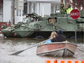 Soldiers in an armoured vehicle drive past a row boat.