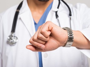 In this stock photo, a doctor wearing a stethoscope checks the time on his wristwatch.