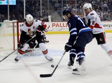 Winnipeg Jets' Adam Lowry (17)  drives towards the net between Ottawa Senators' Erik Karlsson (65) and Dion Phaneuf (2) during first period NHL hockey action in Winnipeg, Sunday, December 3, 2017.