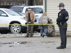 An officer stands guard as people comfort each other near the scene of a fatal shooting at a car wash in Melcroft, Pa., Sunday, Jan. 28, 2018.