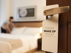 In this stock photo, a maid cleans a hotel room with a make up my room sign on the door.