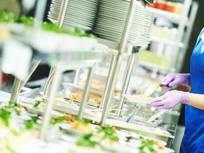 In this stock photo, a worker plates food in a cafeteria.