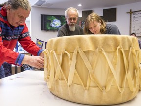 Craftsman Pinock (C) from Kitigan Zibi and Thomas Louttip (L) assist students, including Rheanna Aird (R), in the construction of a traditional grandfather drum at the Mamidosewin Centre within Algonquin College. March 19,2018.