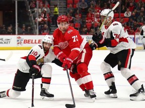 Dylan Larkin #71 of the Detroit Red Wings battles for the puck with Tom Pyatt #10 and Mark Borowiecki #74 of the Ottawa Senators during the first period at Little Caesars Arena on March 31, 2018 in Detroit, Michigan.