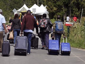 A family from Haiti approach a tent in Saint-Bernard-de-Lacolle, Quebec, stationed by Royal Canadian Mounted Police, as they haul their luggage down Roxham Road in Champlain, N.Y., Monday, Aug. 7, 2017. (AP Photo/Charles Krupa)