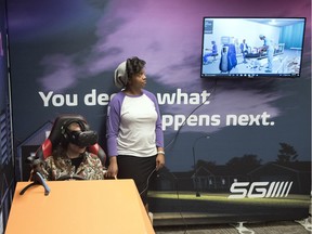 Toni-Tiara Rapley, SGI community relations coordinator, assists Leader-Post reporter Ashley Martin with a virtual reality simulation of impaired driving in Regina. On the TV screen is a view from the VR headset, showing a hospital emergency room following a collision.